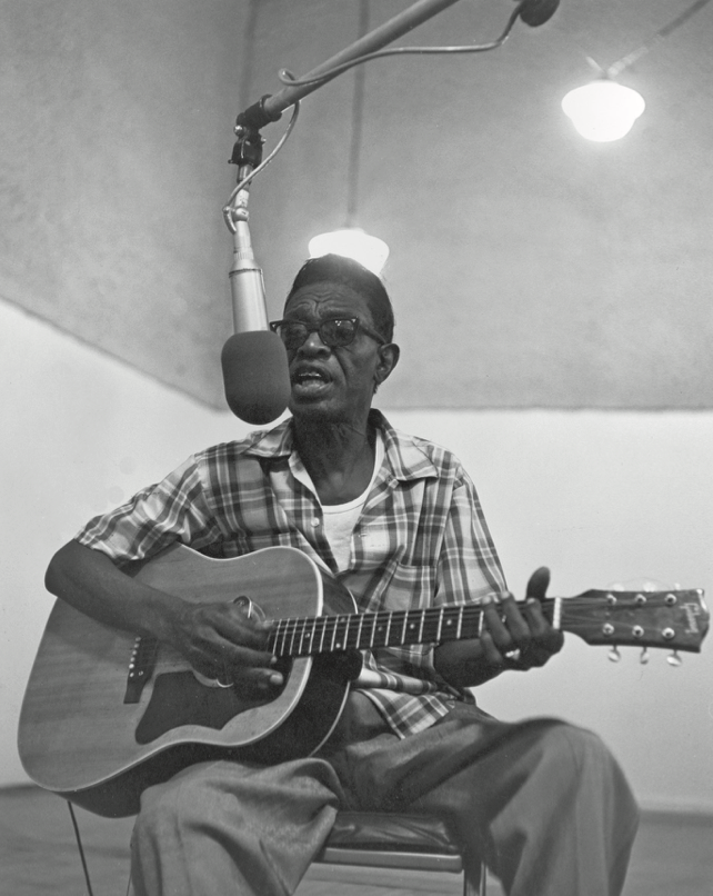 Sam "Lightnin" Hopkins playing guitar and singing into a mic at a studio