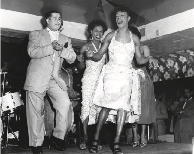 A black and white photo of a group of people singing and dancing on a stage, presumably in a jazz club