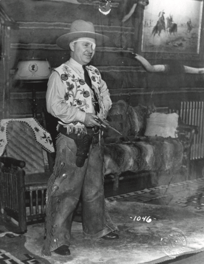 Willy Post dressed in a cowboy getup including chaps, a revolver, vest, eyepatch, and cowboy hat