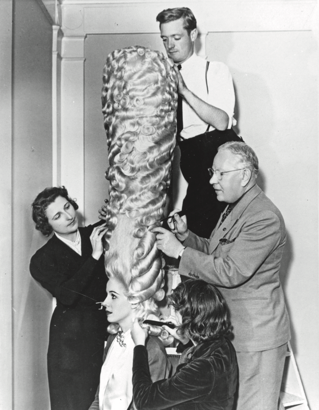 Max Factor and three technicians craft a giant hairpiece on a model.