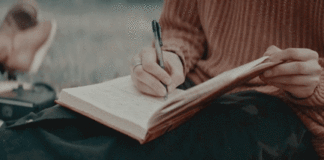 An image of a person in a sweater writing in a journal on their lap
