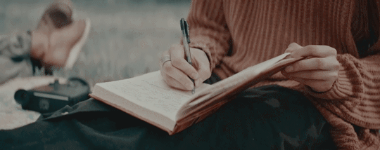An image of a person in a sweater writing in a journal on their lap