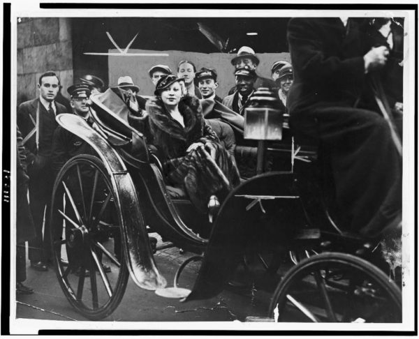 Mae West riding home in her carriage surrounded by fans and paparazzi.